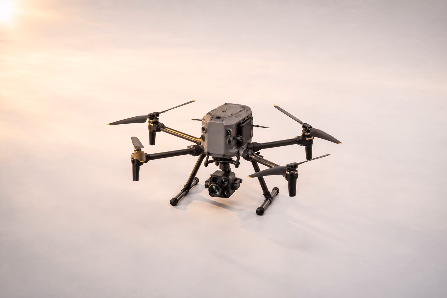 App-Entwicklungsagentur für B2B 17 Graue Hexacopter-Inspektionsdrohne mit sechs Rotorarmen, goldfarbenen Propeller-Spitzen und großem Multilinsen-Kamerasystem am Gimbal auf hellem Studio-Boden – warmes Seitenlicht von links